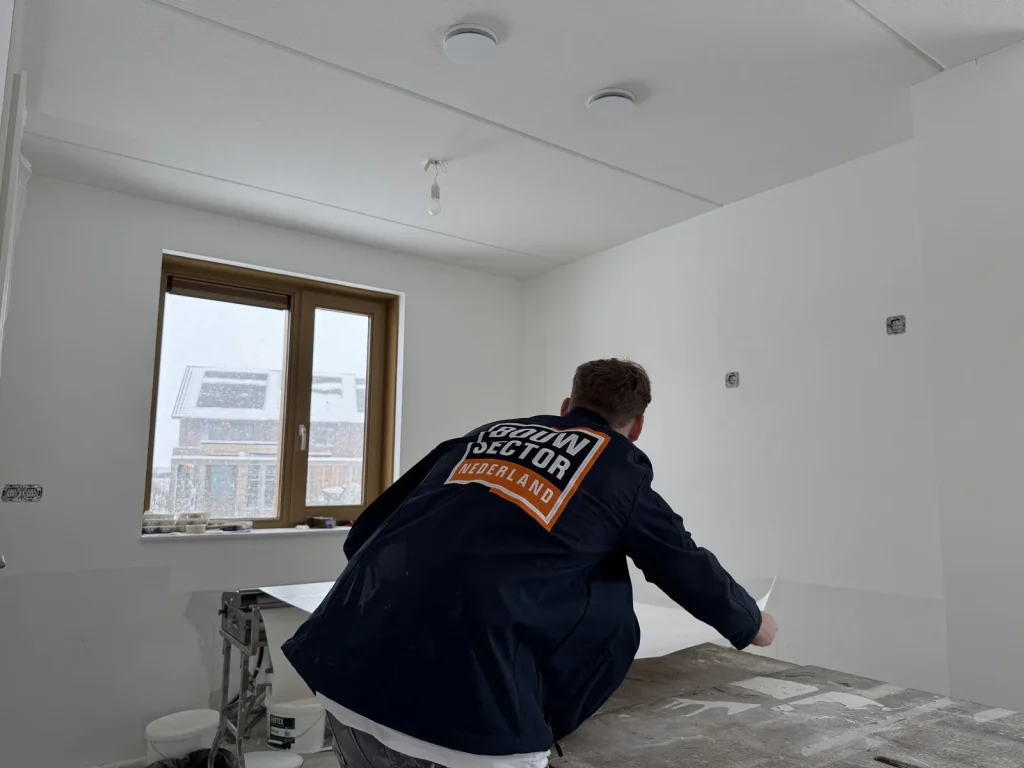 Behanger van Bouwsector Nederland rolt een baan vlies uit op de plaktafel in een kale nieuwbouwkamer