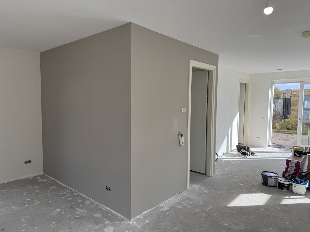 Gesausde vlieswanden in grijs en wit in een nieuwe woning, met verfemmers op de betonvloer