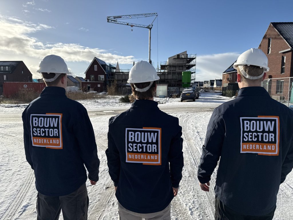 Drie medewerkers van Bouwsector Nederland in werkjassen kijken naar huizen in aanbouw