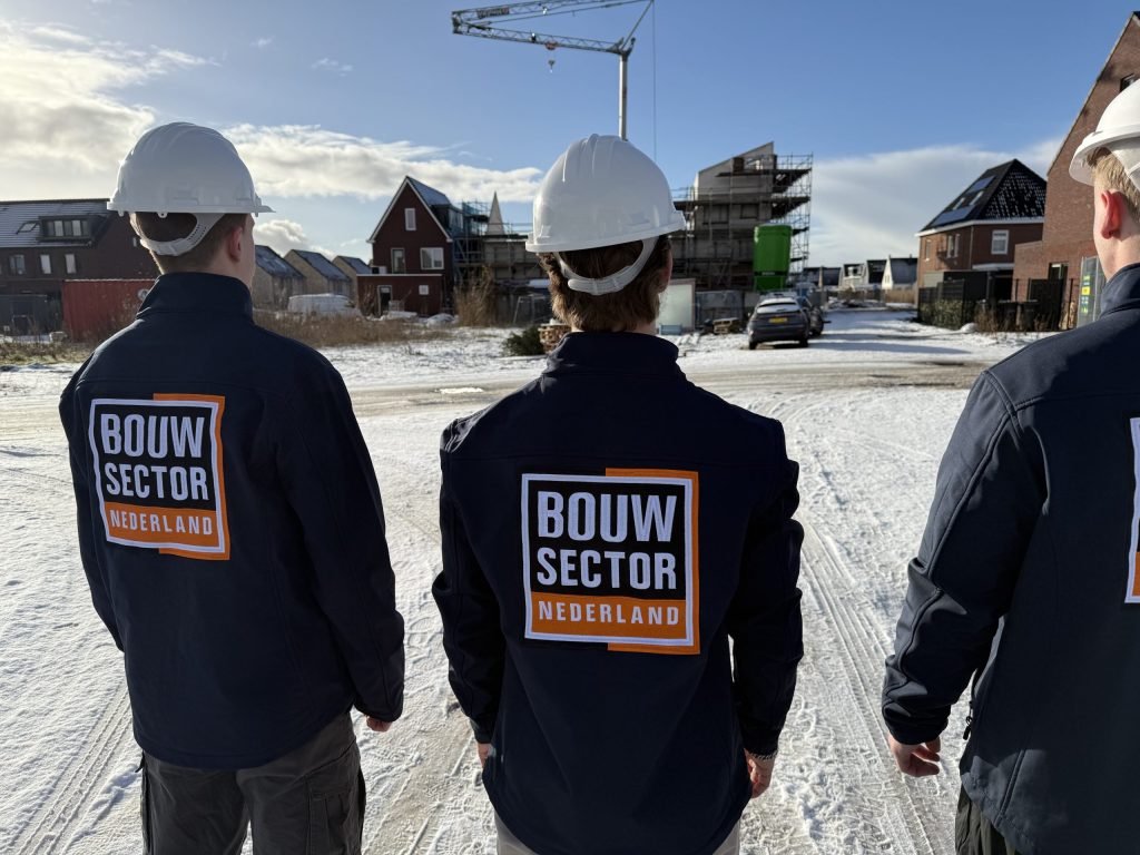Drie vakmensen van Bouwsector Nederland met witte helmen op een besneeuwde nieuwbouwstraat