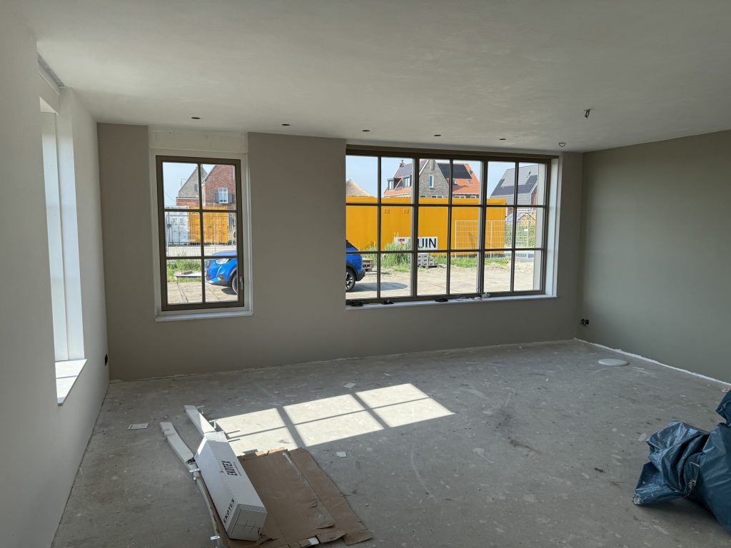Woonkamer in een nieuw huis met twee sprossenramen, zandkleurig gesausde wanden en een kale betonvloer